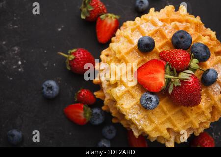Deliziosi waffle con frutti di bosco freschi su una superficie scura Foto Stock