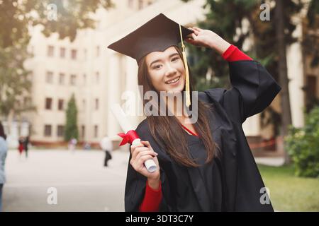 Giovane donna celebra la laurea in un cortile universitario con il diploma in mano Foto Stock