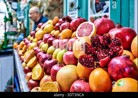 Nella città vecchia di Gerusalemme, un chiosco di frutta offre una varietà di frutta fresca come melograni e arance. I clienti sfogliano la selezione. Foto Stock