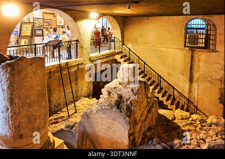 I visitatori camminano attraverso il Cardo nel quartiere ebraico di Gerusalemme, osservando antiche rovine e opere d'arte. La zona è piena di gente. Foto Stock
