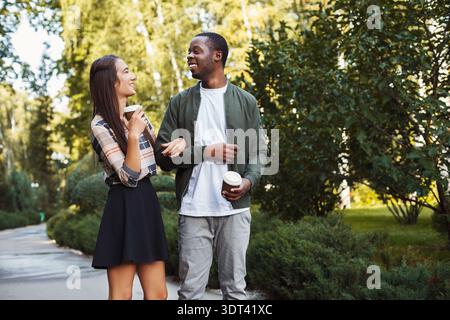 La coppia si gode una passeggiata informale nel parco sorseggiando un caffè durante il caldo pomeriggio Foto Stock