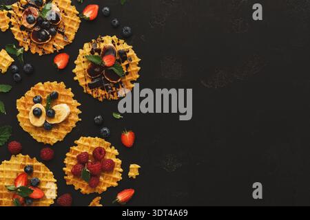 Dessert a base di waffle con frutta e cioccolato disposti in modo giocoso su una superficie scura Foto Stock