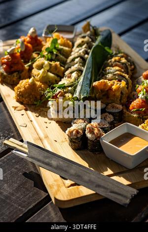 Un ampio e ben organizzato piatto di sushi roll giapponesi assortiti serviti su un grande tavolo di bambù. Il set include una varietà di maki, uramaki, Foto Stock