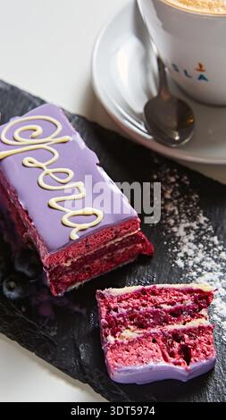 Fetta di torta Opera con vivace glassa viola, delicata calligrafia al cioccolato bianco Foto Stock