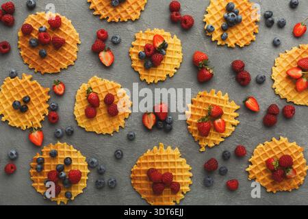 Waffle decorati con vari frutti di bosco su una superficie grigia disposti in stile collage Foto Stock