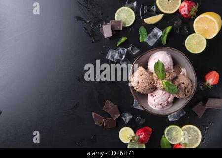 Ampia scelta di gelati in una ciotola con frutta, cioccolato e menta su una superficie scura Foto Stock