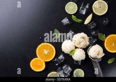 Gelato cremoso con fette di arancia, lime, foglie di menta e cubetti di ghiaccio su superficie nera Foto Stock