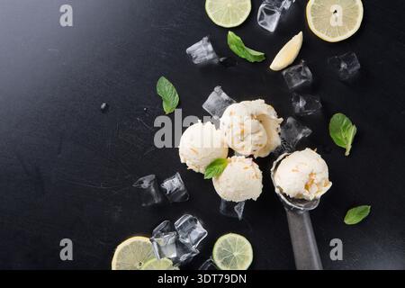 Cucchiaio per gelato con fette di limone e foglie di menta sul tavolo nero con cubetti di ghiaccio Foto Stock