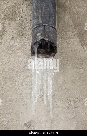 Il vecchio tubo di scarico con acqua congelata contro il muro Foto Stock