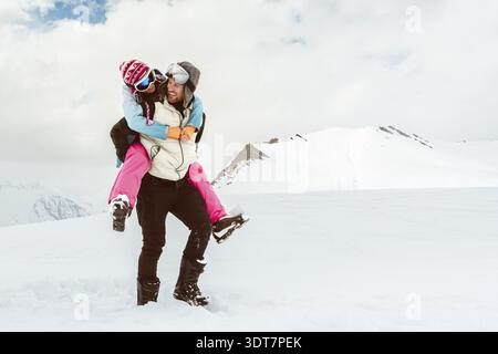 Gioiosa giovane coppia amorevole cammina in piggyback sorridente nella neve profonda condividi legame romantico su montagne innevate, amore, felicità, libertà, relazioni giocose Foto Stock