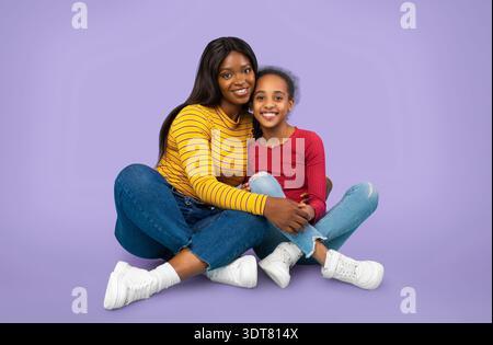 Due persone siedono insieme su uno sfondo viola mentre sorridono e si divertono l'una con l'altra Foto Stock
