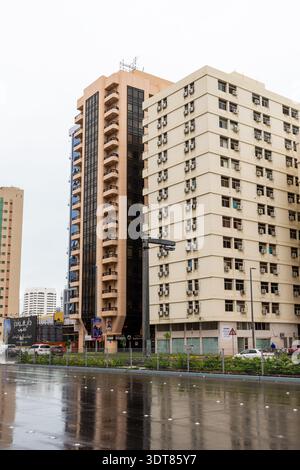Una strada bagnata che mostra chiari riflessi di edifici di appartamenti alti in una giornata nuvolosa e piovosa ad Abu Dhabi, Emirati Arabi Uniti. Foto Stock