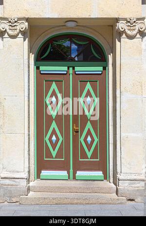 Porte doppie decorative marroni e verdi con poppa ad arco, incorniciate da architettura in pietra Foto Stock