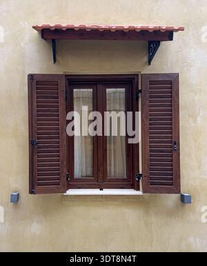 La facciata dell'edificio presenta una vecchia finestra con persiane marroni e una piccola tenda Foto Stock