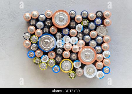 Primo piano delle estremità positive di batterie colorate scariche di dimensioni e formati diversi, vista dall'alto. Batteria alcalina usata su sfondo in cemento. Concetto di spazzatura pericolosa. Foto Stock