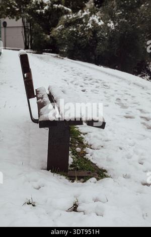Panca in legno ricoperta di neve su un prato innevato. L'immagine fa parte di una serie scattata in Trentino durante una giornata nevosa Foto Stock