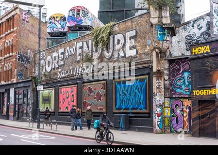 Graffiti Street art sulla Great Eastern Street, Shoreditch, inclusi due vecchi treni sotterranei sopra la strada. Adoriamo e resistiamo a vicenda Foto Stock