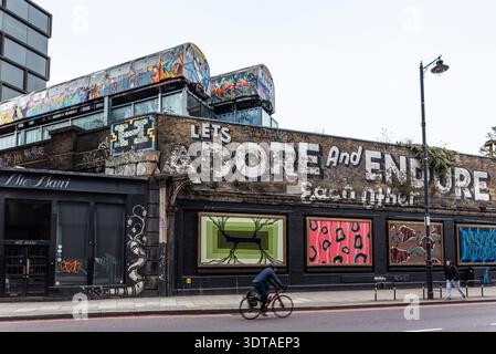 Graffiti Street art sulla Great Eastern Street, Shoreditch, inclusi due vecchi treni sotterranei sopra la strada. Adoriamo e resistiamo a vicenda Foto Stock