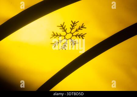 un sole giallo-oro che tramonta, emettendo un caldo bagliore. Al centro, la delicata silhouette nera di un fiocco di neve contrasta nettamente con la schiena vibrante Foto Stock