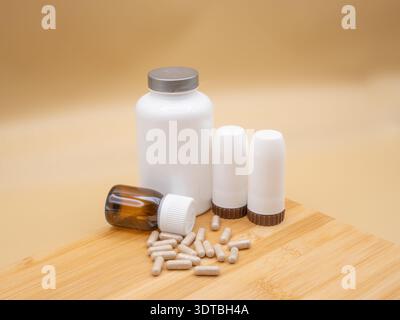 Capsule che fuoriescono da una bottiglia ambrata con vari altri contenitori di integratori su una superficie di legno, promuovendo la salute Foto Stock