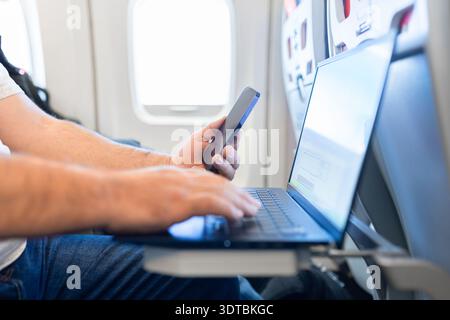 Primo piano di mani maschili che scrivono sul laptop durante il volo in aereo Foto Stock
