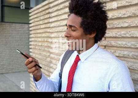 Giovane energico in un abbigliamento da lavoro che si gode una pausa all'aperto e si impegna con i messaggi Foto Stock