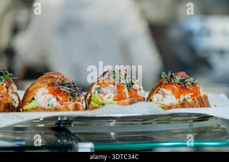 Elegante caffetteria con croissant in barca ripieni di insalata e conditi con uova di salmone e germogli, moderno concetto di snack delicatessen con un'atmosfera soffusa Foto Stock
