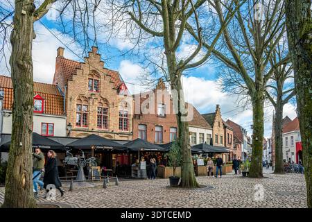 Bruges, Belgio - 14 febbraio 2026: Persone che camminano davanti a case storiche e alla statua di Zeus, Leda, Prometeo e Pegaso a Walplein a Bruges. Foto Stock