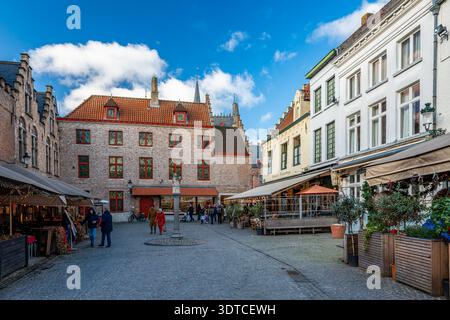 Bruges, Belgio - 14 febbraio 2026: Visitatori che camminano attraverso Huidenvettersplein, conosciuta anche come Piazza dei conciatori, circondata da uno storico edificio in mattoni Foto Stock