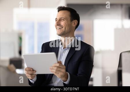 Impiegato ispanico che gode di buone notizie tenendo un tablet in ufficio Foto Stock