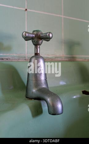Vecchio rubinetto d'acqua metallico in un lavandino in ceramica verde vintage con piastrelle sullo sfondo Foto Stock