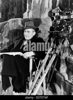 Leo McCarey, vincitore dell'Oscar, viene catturato seduto sul set negli anni '1930, accanto a una telecamera cinematografica. Indossa una fedora, un cappotto e una cravatta a motivi, suggerendo un momento di contemplazione creativa durante una produzione cinematografica. Foto Stock