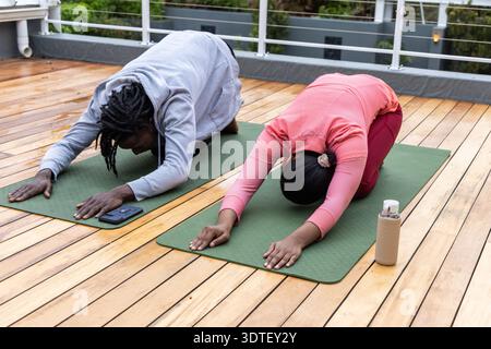 Coppia afroamericana che fa bambini posare su tappeti verdi sul tetto di legno, telefono a sinistra, bottiglia a destra Foto Stock