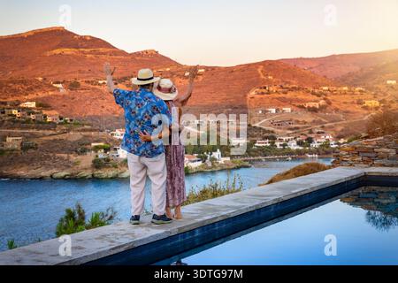 Una coppia felice e anziana in vacanza si trova accanto alla piscina e gode della vista del tramonto Foto Stock
