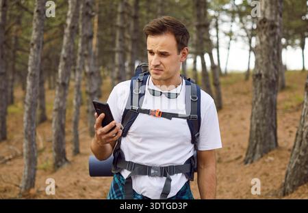 Escursionista che controlla il segnale dello smartphone perso nella foresta, cercando di trovare la geolocalizzazione Foto Stock