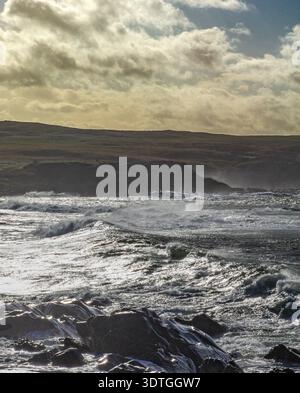 La luce del sole che si infrangono tra le nuvole sulle onde dell'Atlantico e sulla costa rocciosa della penisola di Inishowen, contea di Donegal, Irlanda. Foto Stock