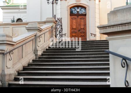 Un'ampia scalinata in pietra intemprata con ringhiere decorative sale verso una porta doppia in legno antico splendidamente lavorata all'interno di una entr ad arco Foto Stock