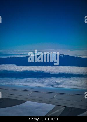 Vista del vulcano del Monte Teide che si innalza sopra una coperta di nuvole, vista dalla finestra di un aereo. Cima innevata e paesaggio vulcanico di Tenerife cr Foto Stock