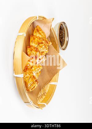 Appetitoso cibo asiatico. Gnocchi fritti dorati croccanti serviti in una vaporiera di bambù con salsa di soia scura. Composizione minimalista con luminoso, cle Foto Stock