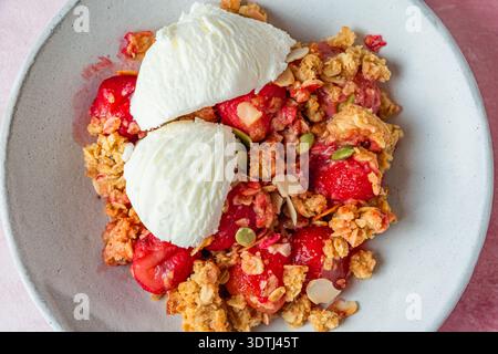 Crumble di fragole con sessole per gelato, muesli al forno, semi di zucca e mandorle nel recipiente. Dessert di frutta croccante estivo. Pasta dolce fatta in casa con Foto Stock