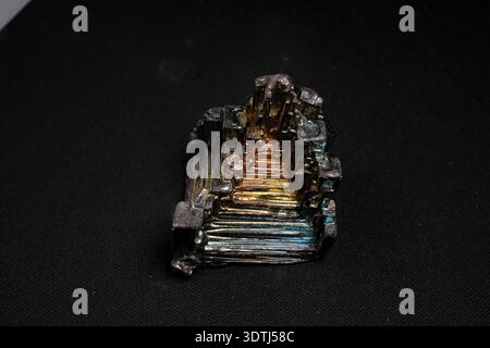 Cristallo di bismuto iridescente con terrazze metalliche a gradini su sfondo nero Foto Stock