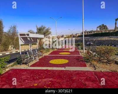 Marciapiede in cemento dipinto di rosso e giallo sulla strada per il vecchio mercato di Sharm El Sheikh (Egitto). Strada cittadina con panchine e palme Foto Stock