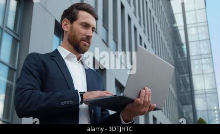 Serio uomo d'affari caucasico maturo con notebook in città tipizzazione uomo d'affari sviluppatore maschio che scrive computer avvio online che chatta utilizzando Foto Stock