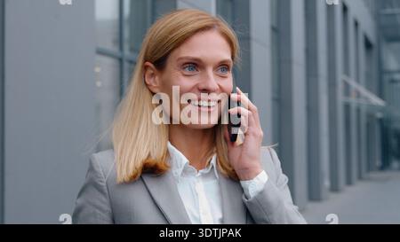 Felice soddisfatto donna d'affari caucasica adulta che parla telefonicamente amichevole discutere successo donna d'affari di mezza età specialista donna all'aperto Foto Stock