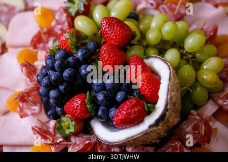 Salumi gourmet con salumi, fragole fresche, uva in guscio di cocco. Display tropicale creativo, pratico e delizioso per ospitare Foto Stock