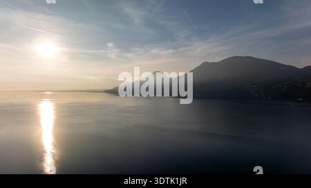 Una serena vista serale del Lago di Garda con il sole che tramonta sulla zona di Brenzone, che emette un caldo bagliore e si riflette sulle tranquille acque del Nord Foto Stock