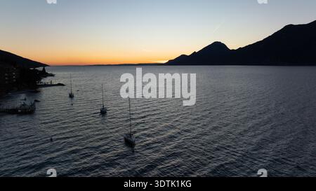 Tranquillo tramonto sul Lago di Garda a Brenzone, con acque tranquille e sagome delle Alpi italiane. Il tranquillo cielo serale riflette una miscela di orano Foto Stock