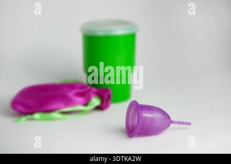 Tazza mestruale viola appoggiata su una superficie pulita con un contenitore verde e una custodia rosa, per un'igiene sostenibile. Foto Stock