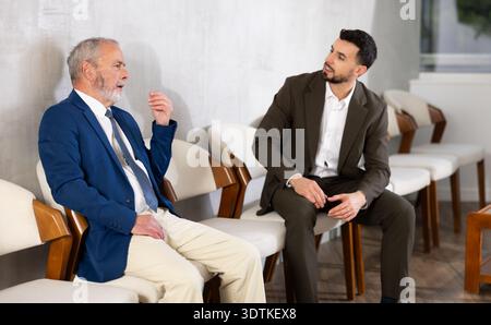 Uomini giovani e anziani che parlano in attesa di un colloquio di lavoro Foto Stock