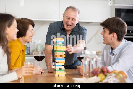 Un anziano sorridente o un padre che si divertono a giocare nella costruzione della torre con la moglie e i bambini adulti in una comoda casa di famiglia Foto Stock